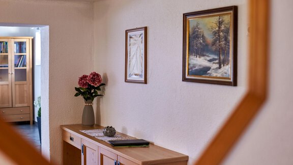 Ein helles Zimmer mit einem Holzsideboard und einer Vase mit Blumen. An der Wand hängen zwei Bilder, die eine ruhige Atmosphäre schaffen. - Ferienhaus Schrankogelblick - Längenfeld