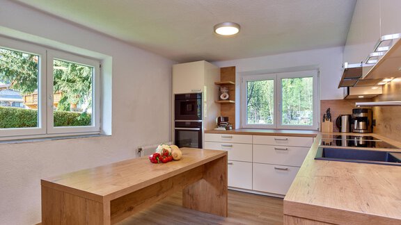 Eine moderne Küche mit hellen Wänden und Holzmöbeln. Auf dem Tisch liegen Obst und das Sonnenlicht scheint durch die Fenster. - Ferienhaus Schrankogelblick - Längenfeld
