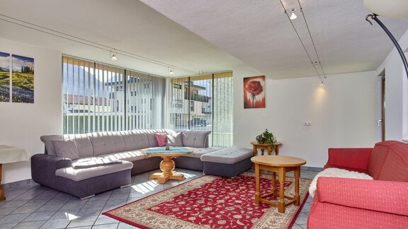 Ein helles Wohnzimmer mit großen Fenstern und modernen Möbeln. Es gibt eine gemütliche Sitzecke und einen Teppich auf dem Boden. - Ferienhaus Schrankogelblick - Längenfeld