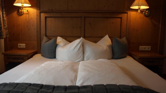 Ein gemütliches Schlafzimmer mit einem großen Bett und weichen Kissen. Sanftes Licht von den Wandleuchten schafft eine entspannte Atmosphäre. - Ferienhaus Schrankogelblick - Längenfeld