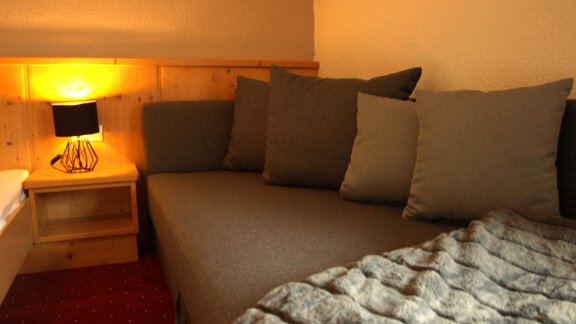 Ein gemütliches Wohnzimmer mit einem grauen Sofa und vielen Kissen. Neben dem Sofa steht ein kleiner Tisch mit einer Lampe. - Ferienhaus Schrankogelblick - Längenfeld