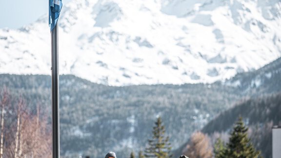 Eine Gruppe von vier Personen geht an einem Geländer entlang, mit schneebedeckten Bergen im Hintergrund. Der Himmel ist klar und sonnig. - Ferienhaus Schrankogelblick - Längenfeld