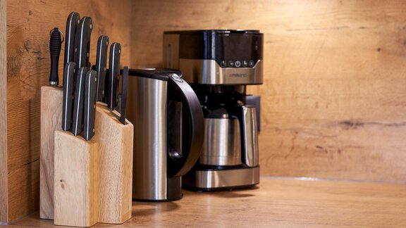 A modern kitchen corner with a knife block and a coffee machine. The wooden background creates a warm atmosphere. - Ferienhaus Schrankogelblick - Längenfeld