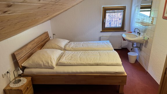 Ein gemütliches Schlafzimmer mit zwei Betten und einem kleinen Tisch. Es gibt ein Fenster und ein Waschbecken, alles in einem einfachen, rustikalen Stil. - Ferienhaus Volgger - Längenfeld