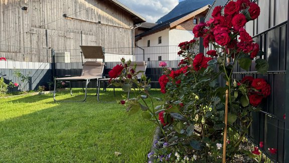 Ein schöner Garten mit roten Rosen und einem Rasen. Im Hintergrund sind Holzgebäude und Berge zu sehen. - Ferienhaus Volgger - Längenfeld