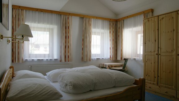Ein helles Schlafzimmer mit einem großen Bett und weißen Kissen. Fenster mit Vorhängen sorgen für eine freundliche Atmosphäre. - Ferienhaus Volgger - Längenfeld