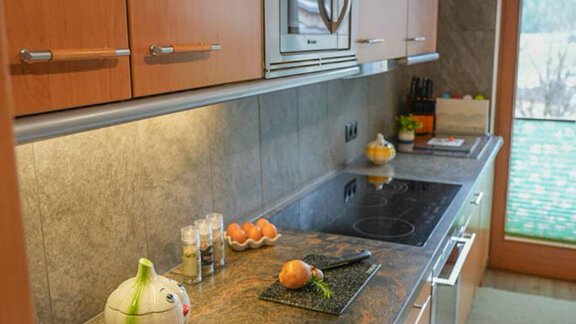 A modern kitchen with wooden cabinets and an elegant stone countertop. On the work surface, some fruits and spices are visible. - Hauertalerhof - Längenfeld
