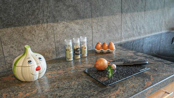A modern kitchen with a granite countertop. On the table, there is a knife, an onion, eggs, and spices in jars. - Hauertalerhof - Längenfeld