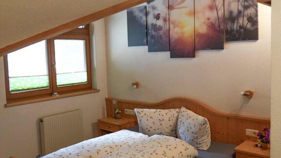 A cozy bedroom with a sloping roof and wooden furniture. On the wall hang pictures of a sunset landscape. - Hauertalerhof - Längenfeld