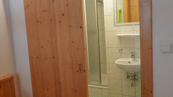 A bright room with an open wooden sliding door that leads to a bathroom. The bathroom has tiles and a shower. - Hauertalerhof - Längenfeld
