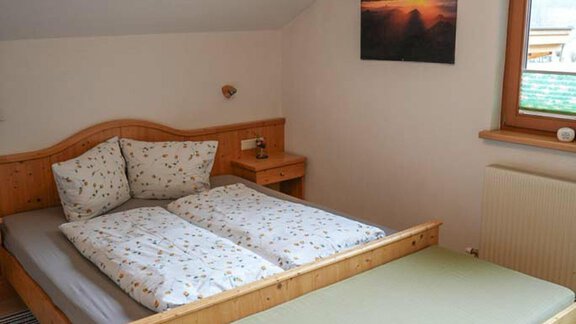 A cozy bedroom with a large bed and colorful pillows. The room has a window looking outside as well as a picture on the wall. - Hauertalerhof - Längenfeld