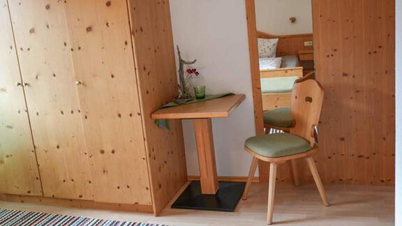 A simple bedroom with wooden furniture and a large mirror. The room is designed to be bright and welcoming. - Hauertalerhof - Längenfeld