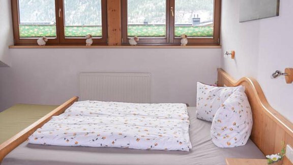 A cozy bedroom with a wooden bed and large windows. The room has a warm, inviting atmosphere. - Hauertalerhof - Längenfeld
