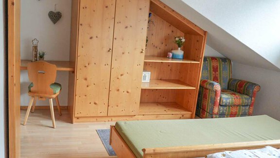 A cozy room with wooden furniture and a skylight. There is a bed, a desk, and a seating area. - Hauertalerhof - Längenfeld