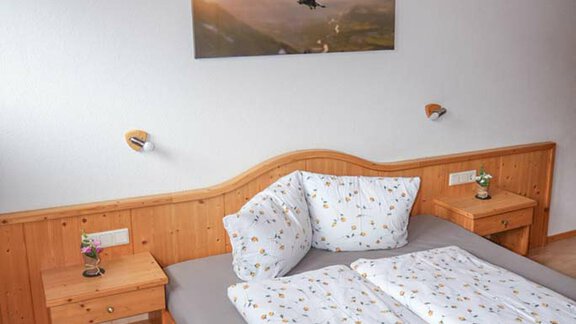 A cozy bedroom with a wooden frame bed and colorful bed covers. On the wall hangs a picture of birds in nature. - Hauertalerhof - Längenfeld
