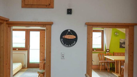A bright room with wood paneling and two open doors. On the left side, there is a sofa and on the right side, a dining area with a table and chairs. - Hauertalerhof - Längenfeld