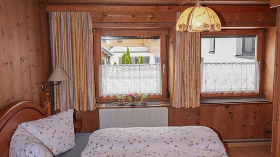 A cozy bedroom with wood paneling and a large bed. The windows let in plenty of daylight and create an inviting atmosphere. - Hauertalerhof - Längenfeld
