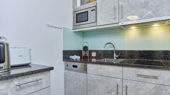 A modern kitchen unit with gray cabinets and stainless steel appliances. The equipment includes a microwave, sink, and dishwasher. - Haus Klaudia Gstrein - Längenfeld