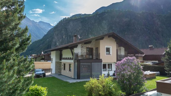 A cozy house in a green environment with mountains in the background. The garden is well-maintained and there is a blooming plant in front of the house. - Haus Klaudia Gstrein - Längenfeld