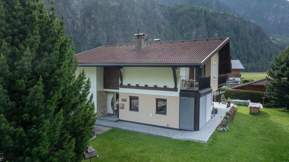 A modern house set in a green environment with mountains in the background. The well-maintained garden surrounds the building and provides an inviting atmosphere. - Haus Klaudia Gstrein - Längenfeld