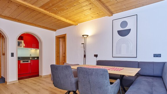 A modern living room with a wooden ceiling and a cozy seating area. The kitchen is done in red and well-equipped. - Haus Klaudia Gstrein - Längenfeld