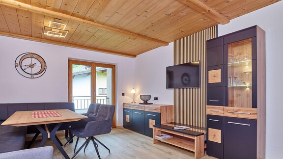 A modern living room with a wooden floor. There is a dining table, a cozy seating area, and a television. - Haus Klaudia Gstrein - Längenfeld