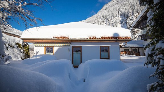 A cozy house nestled in deep snow, surrounded by snow-covered mountains. The sky is clear and blue. - Haus Margret - Längenfeld
