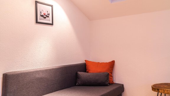 A cozy room with a gray sofa and colorful cushions.  
A small picture hangs on the wall and there is a wooden table next to the sofa. - Haus Viktoria - Längenfeld