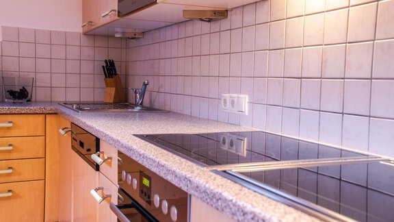 A modern kitchen with wooden cabinets and a smooth work area. The room is bright and well-equipped with cooktops and utensils. - Haus Viktoria - Längenfeld