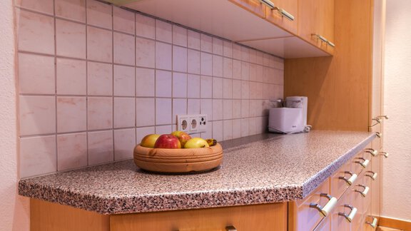 A modern kitchen with a granite countertop. On the work surface, there is a bowl with various fruits. - Haus Viktoria - Längenfeld
