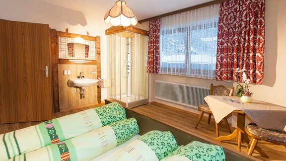 A cozy room with two beds and a small seating area. The bathroom is separated from the living area by a glass partition. - Haus Waldhof - Längenfeld