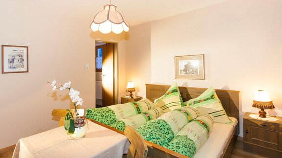 A cozy bedroom with a double bed and green bedding. There is a small table with a flower and warm light from the bedside lamps. - Haus Waldhof - Längenfeld