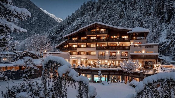 A charming hotel in winter, surrounded by snow-covered mountains. The facade is illuminated and the surroundings are enveloped in a calm, wintry atmosphere. - Hotel Rita - Längenfeld