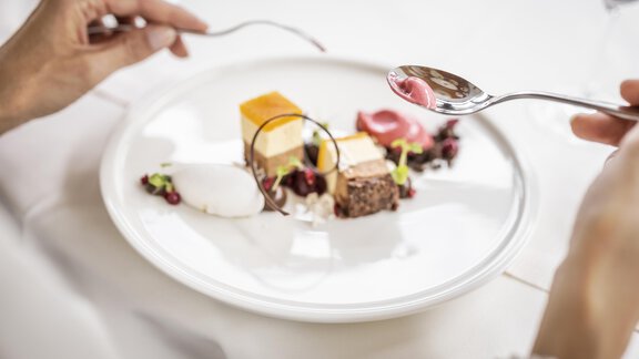 An artistically arranged dessert platter with various treats. Two hands hold spoons, ready to indulge. - Hotel Rita - Längenfeld