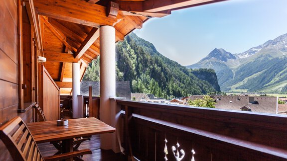 Ein gemütlicher Balkon mit einem Holztisch und Stühlen, umgeben von Bergen und grünen Wäldern. Der klare Himmel bietet einen schönen Ausblick auf die Natur. - Hotel Stern - Längenfeld