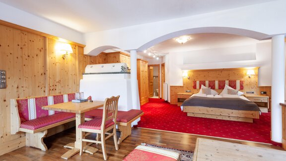 Ein gemütliches Hotelzimmer mit Holzvertäfelung und einem großen Doppelbett. Der Raum ist mit einem Essbereich und einem weichen Teppich ausgestattet. - Hotel Stern - Längenfeld