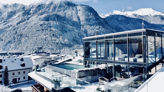 Ein modernes Gebäude mit einem gläsernen Pool, umgeben von verschneiten Bergen. Die Landschaft strahlt Ruhe und Winterzauber aus. - Hotel Stern - Längenfeld