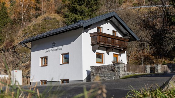 A modern house with a balcony and a white facade. Surrounded by nature and trees, it offers a tranquil atmosphere. - Irmas Ferienhäusl - Längenfeld