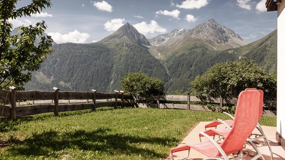 Eine malerische Aussicht auf hohe Berge mit grünen Wiesen. Im Vordergrund stehen Sonnenliegen auf einer Terrasse. - MYALPS Himmelreich - Längenfeld