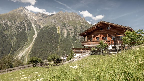 A cozy chalet is situated in a green meadow, surrounded by majestic mountains. The sky is clear and the atmosphere is peaceful. - MYALPS Himmelreich - Längenfeld