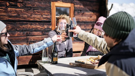 Eine Gruppe von Menschen stößt mit Getränken an, während sie an einem Tisch sitzen. Im Hintergrund ist eine gemütliche Holzlaube zu sehen. - MYALPS Jordans Lodge - Längenfeld