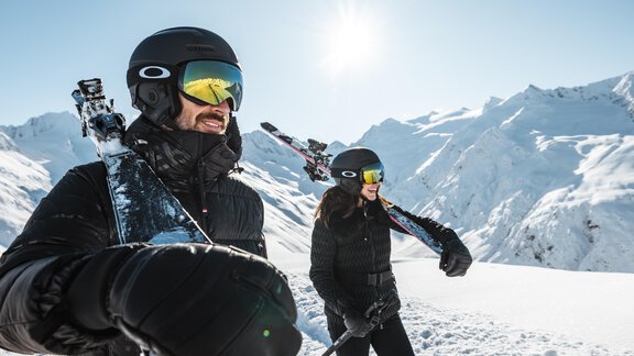 Zwei Skifahrer stehen auf der Piste und blicken auf die verschneiten Berge. Die Sonne scheint hell am blauen Himmel. - MYALPS Jordans Lodge - Längenfeld