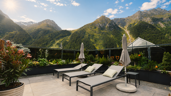 Eine sonnige Terrasse mit Liegestühlen und Blick auf grüne Berge. Bunte Pflanzen ergänzen die idyllische Landschaft. - VIER - Studios & Restaurant - Längenfeld