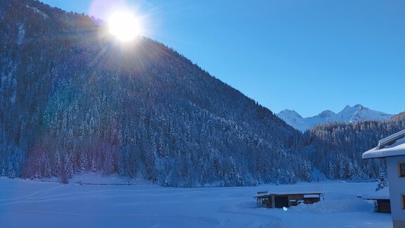 A snow-covered landscape with mountains and a clear blue sky. The sun shines brightly over the snowy scenery. - Apart Alpenflair - Niederthai