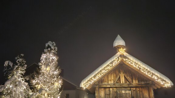 A cozy wooden cabin, surrounded by snow, radiates Christmas lights. In the foreground, there is a festively decorated tree. - Apart Alpenflair - Niederthai