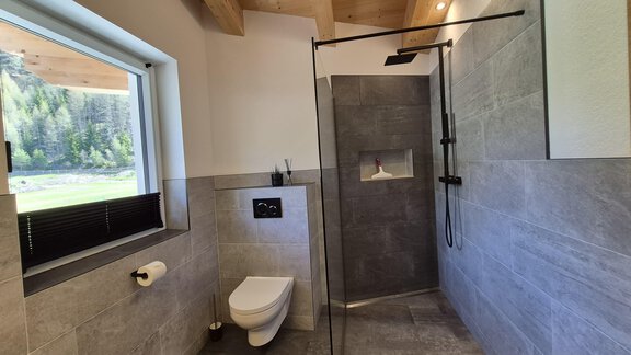 Ein modernes Badezimmer mit Dusche und WC. Große Fenster sorgen für viel natürliches Licht und einen Blick ins Grüne. - Apart Alpenflair - Niederthai