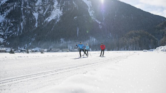 Three skiers glide over a snowy landscape. In the background, majestic mountains and a clear, blue sky can be seen. - Apart Alpenflair - Niederthai