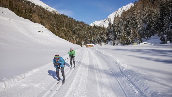 Two people cross-country skiing on a snow-covered trail. In the background, woods and mountains can be seen. - Apart Alpenflair - Niederthai
