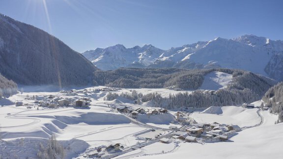 A picturesque winter landscape with snow-covered mountains and a small village. The sun is shining brightly and the sky is clear and blue. - Apart Alpenflair - Niederthai