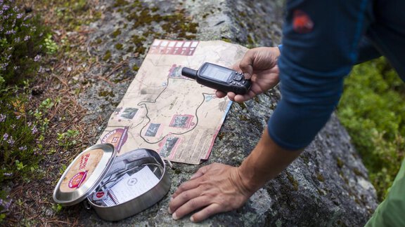 Eine Person betrachtet eine Karte und hält ein GPS-Gerät in der Hand. Der Hintergrund zeigt natürliche Felsen und Pflanzen. - Apart Alpenflair - Niederthai